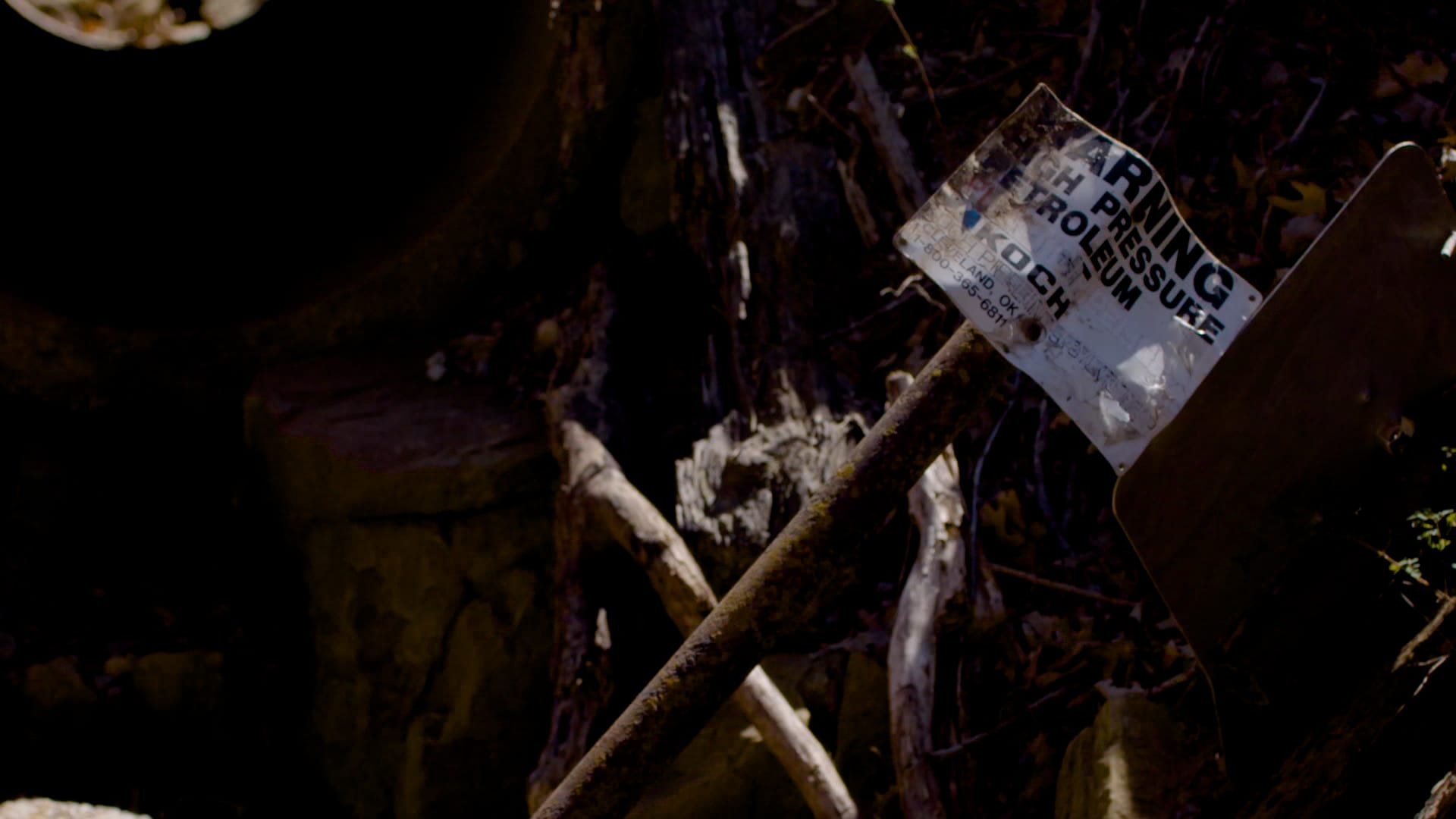 A weathered Koch high-pressure petroleum warning sign fallen in the brush.