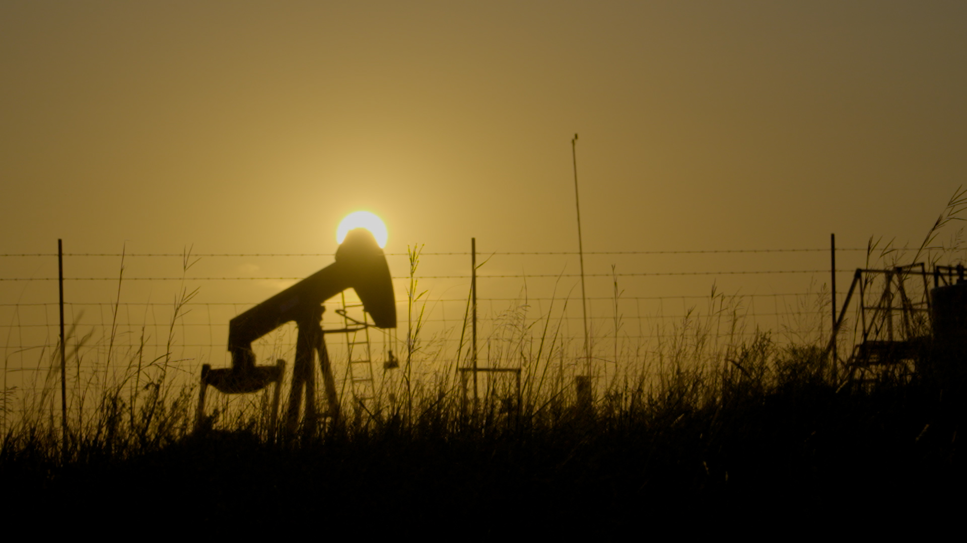 A pump jack silhouetted against a smoky amber sunset on the Osage Reservation.